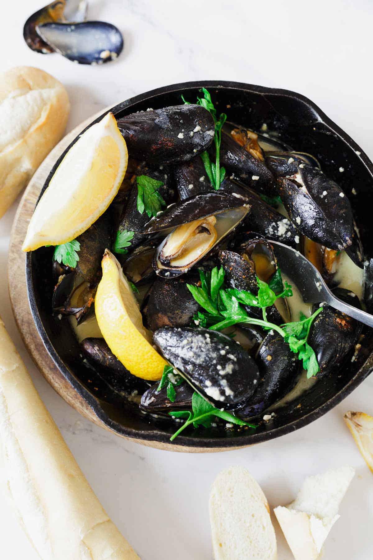 A bowl of steamed mussels in a creamy sauce with lemon wedges, fresh parsley, and baguette slices&mdash;a coastal classic often enjoyed alongside the best vegetarian food in France.