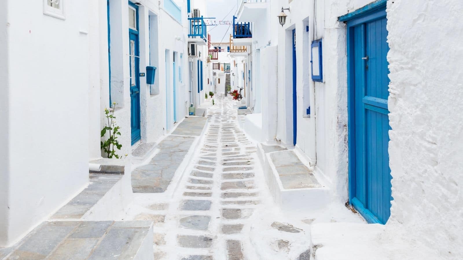 Narrow stone street lined with white buildings and blue doors in a sunlit Greek island village.