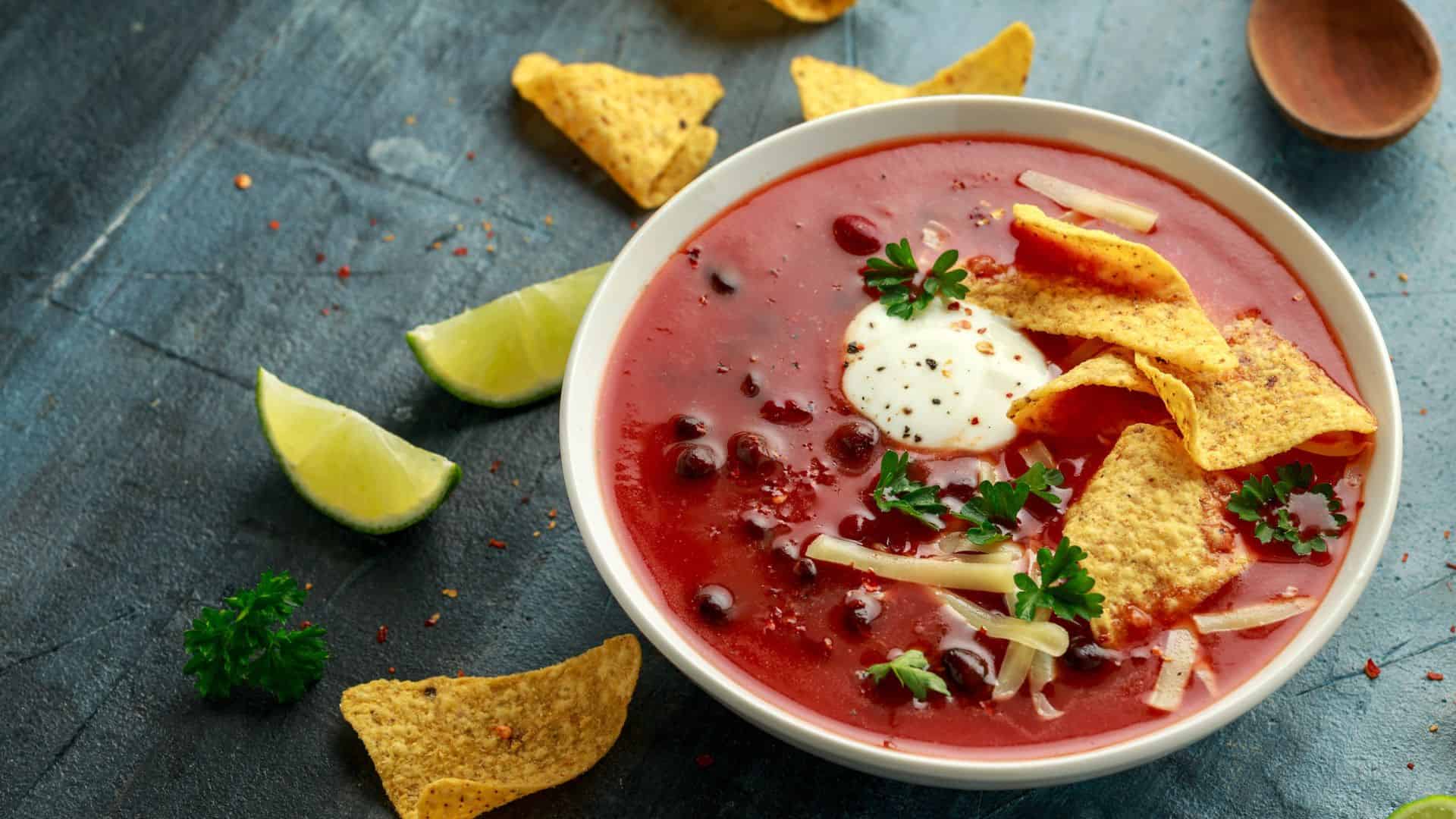 Bowl of tomato soup with tortilla chips, sour cream, cheese, and herbs, with lime wedges on the side&mdash;one of the Best Vegetarian Mexican Dishes to savor.