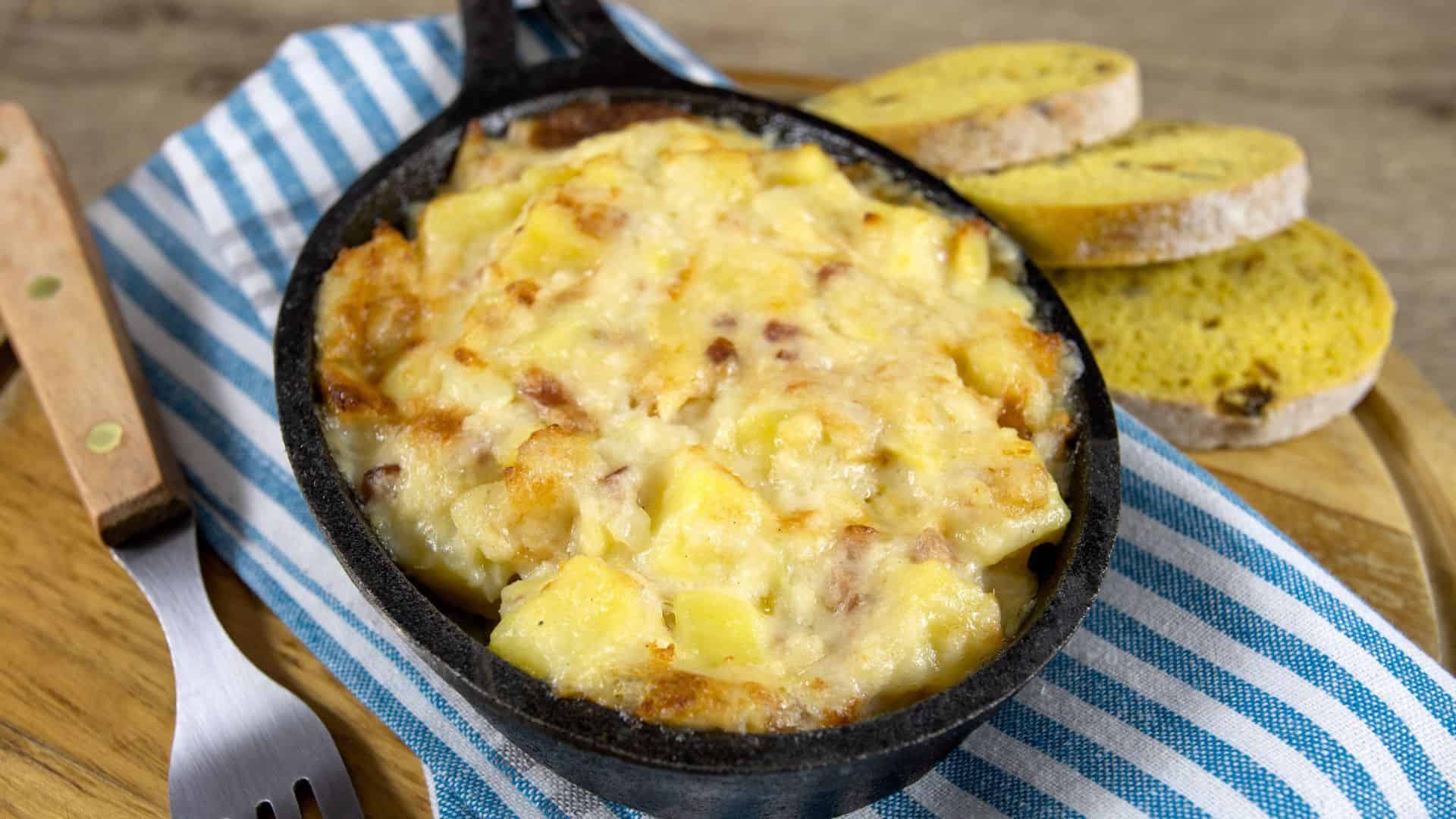 Cheesy baked potato casserole in a cast iron dish, served with sliced bread on a striped cloth&mdash;an inviting example of the Best Vegetarian Food in France.