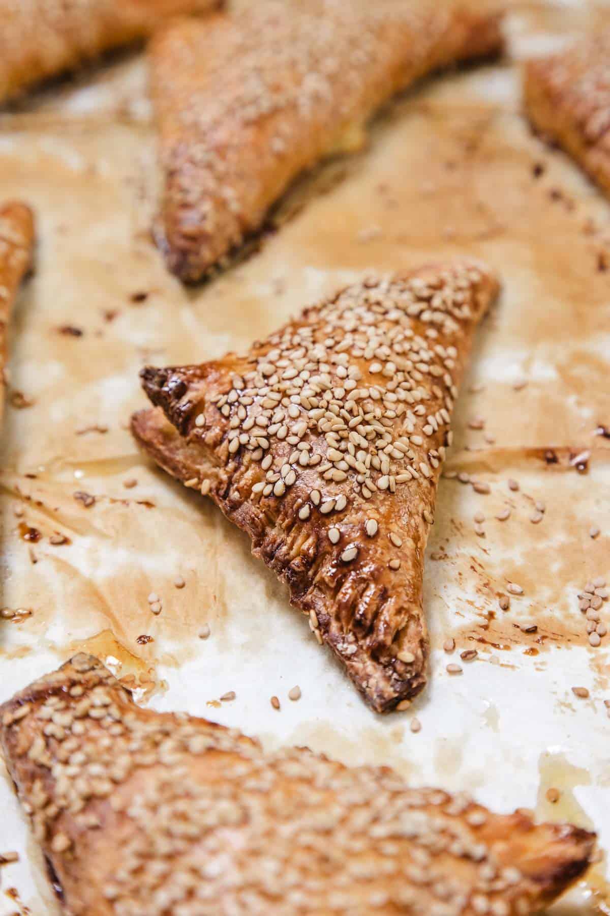 Golden brown triangular pastries topped with sesame seeds on parchment paper, these delightful treats are a staple of vegetarian food in Israel.
