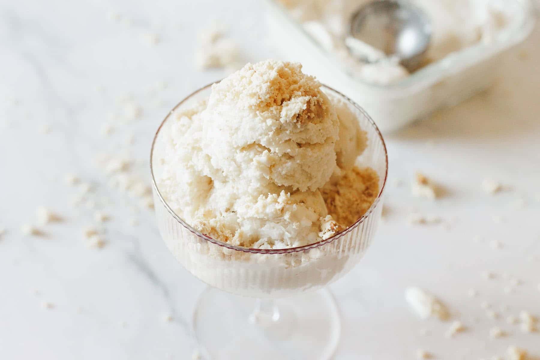A glass filled with scoops of vanilla ice cream topped with crumbled cookie on a marble surface&mdash;a delightful treat inspired by vegetarian food in Israel.