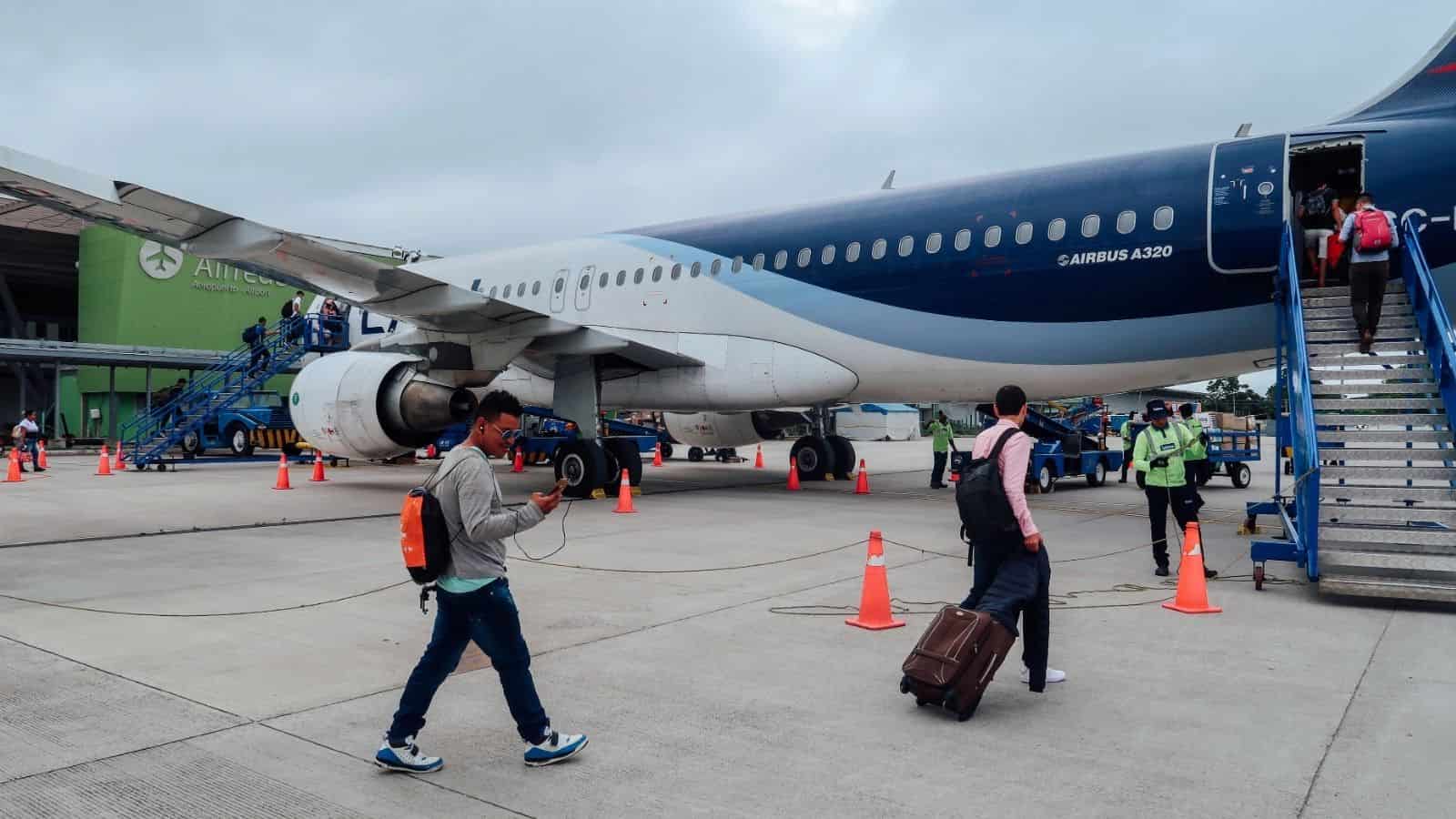 Passengers boarding an Airbus A320 on an airport tarmac, with orange cones and staff nearby.