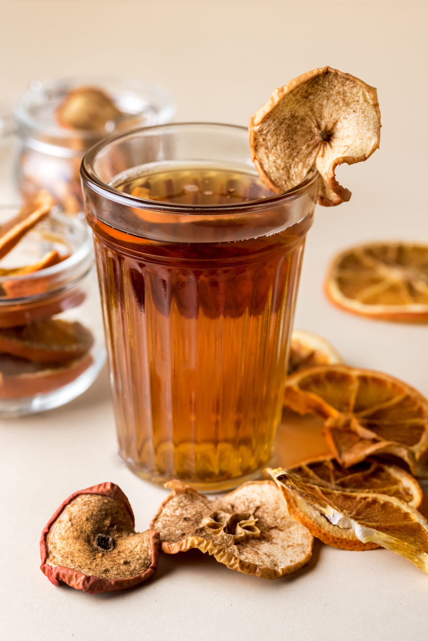A glass of apple tea garnished with a dried apple slice, surrounded by assorted dried fruit&mdash;a delightful example of vegetarian food inspired by Ukraine.