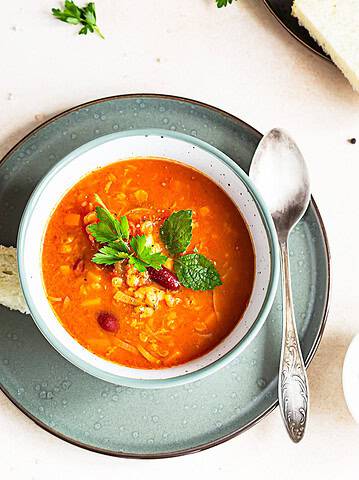 A bowl of Ukrainian vegetable soup with herbs, a classic vegetarian dish, served with bread and a spoon on a plate.