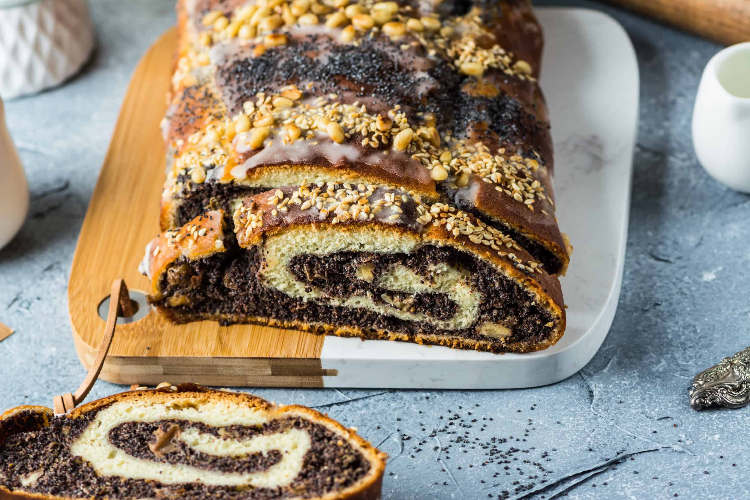 A sliced poppy seed roll, a classic vegetarian Ukrainian food, topped with nuts and icing, served on a white cutting board.