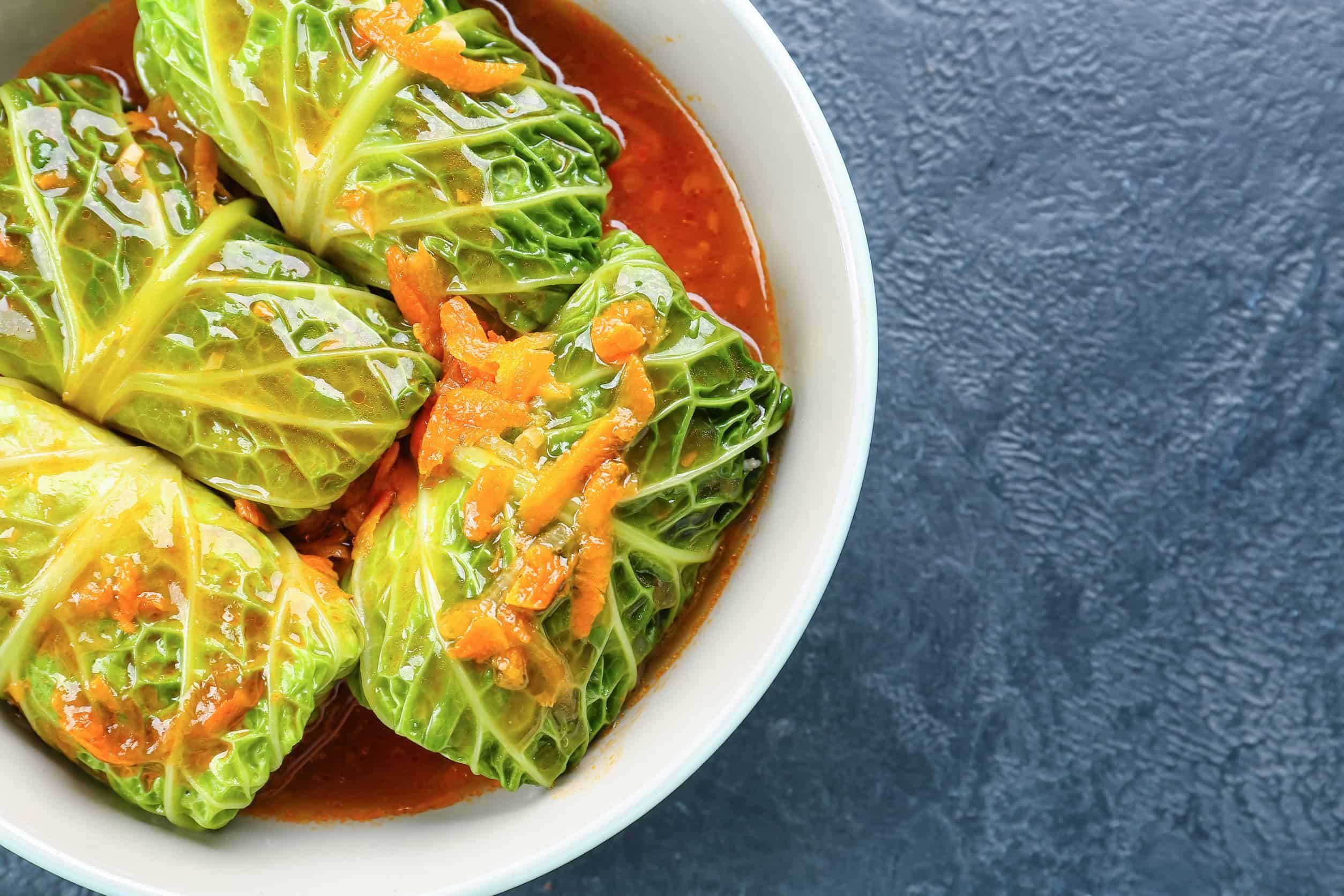 Stuffed cabbage rolls in tomato sauce, a classic example of Ukrainian vegetarian food, served in a white bowl on a textured dark surface.