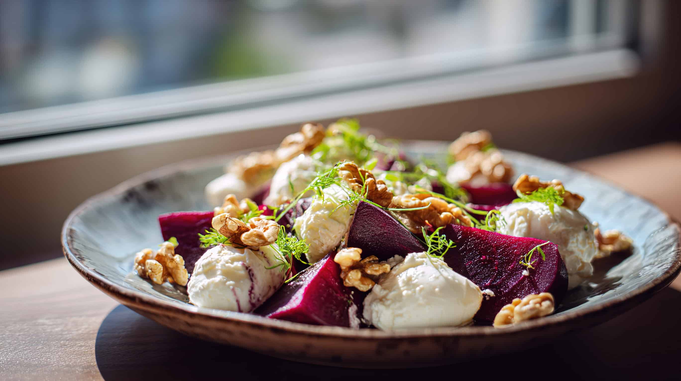 A plate of beet salad with goat cheese, walnuts, and fresh herbs&mdash;a classic Ukrainian vegetarian dish&mdash;sits by a sunny window.