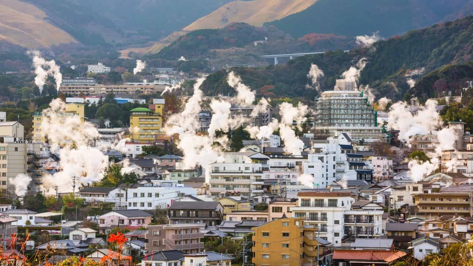 Steam rises from numerous buildings in a Japanese town, surrounded by hills and mountains&mdash;an enchanting scene often found among top Japan summer destinations.