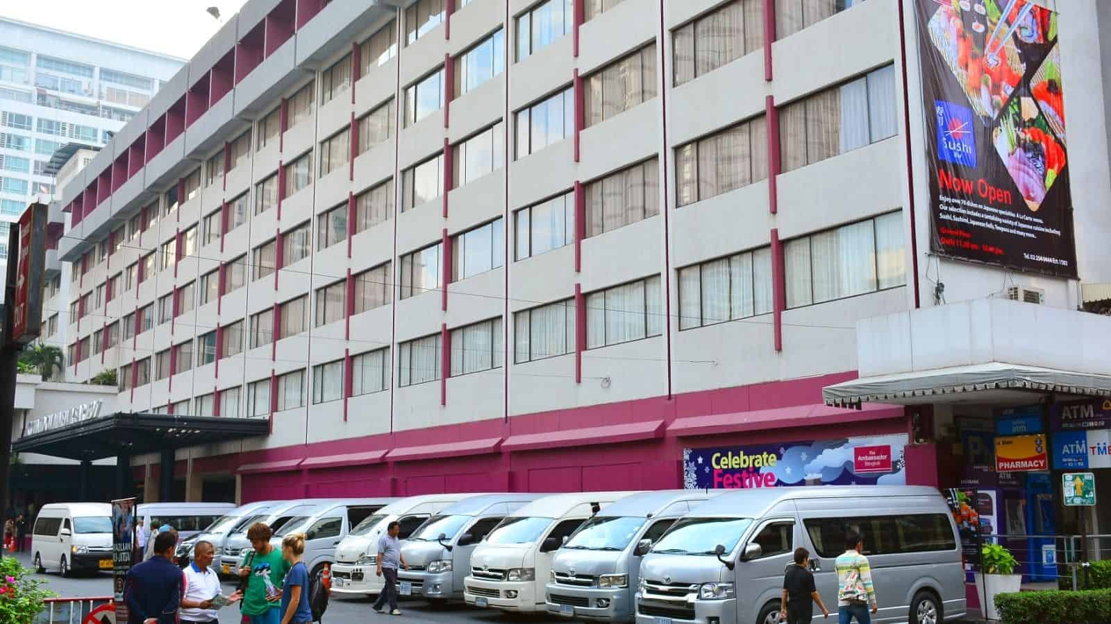 People walk past a row of parked vans in front of a multi-story building with shops at street level, making the most of Asia travel hacks and travel tips to stay comfortable in the hot weather.
