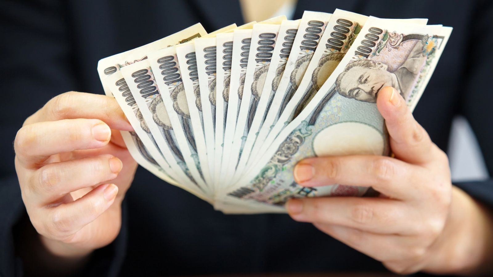 A person holding and fanning out several Japanese 10,000 yen banknotes with both hands.