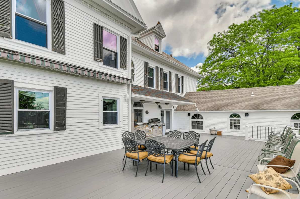 Spacious deck with outdoor dining set, grill, and large white house with black shutters in the background&mdash;perfect for relaxing after a day touring Finger Lakes Wineries with Lodging nearby.