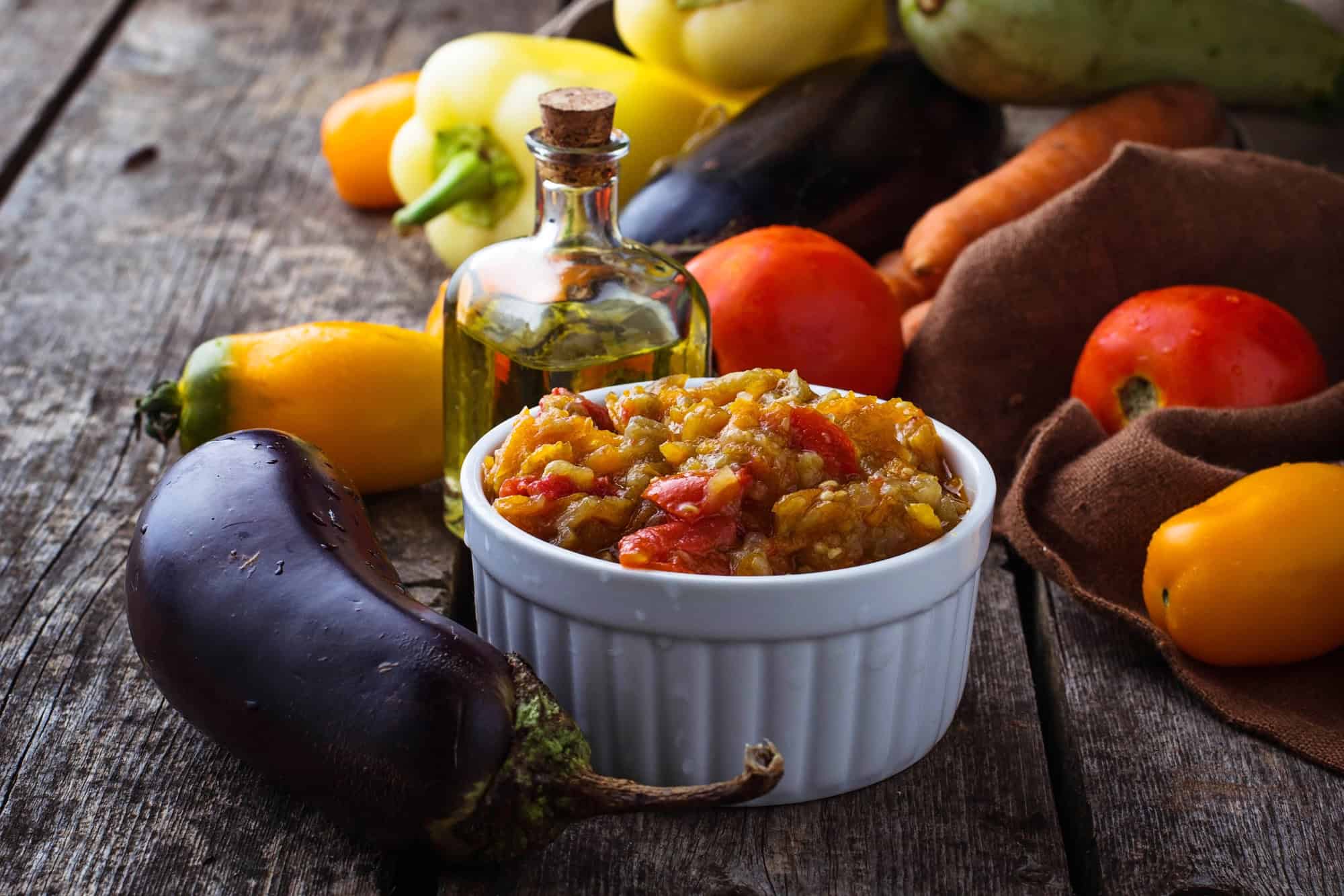 Bowl of vegetable relish on a rustic table, surrounded by fresh vegetables and a bottle of oil&mdash;a classic example of vegetarian dishes in Russia.