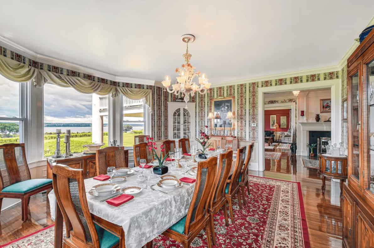 Elegant dining room with a set dining table, large windows, and chandelier, offering serene views of greenery and water&mdash;perfect for guests exploring Finger Lakes Wineries with Lodging nearby.