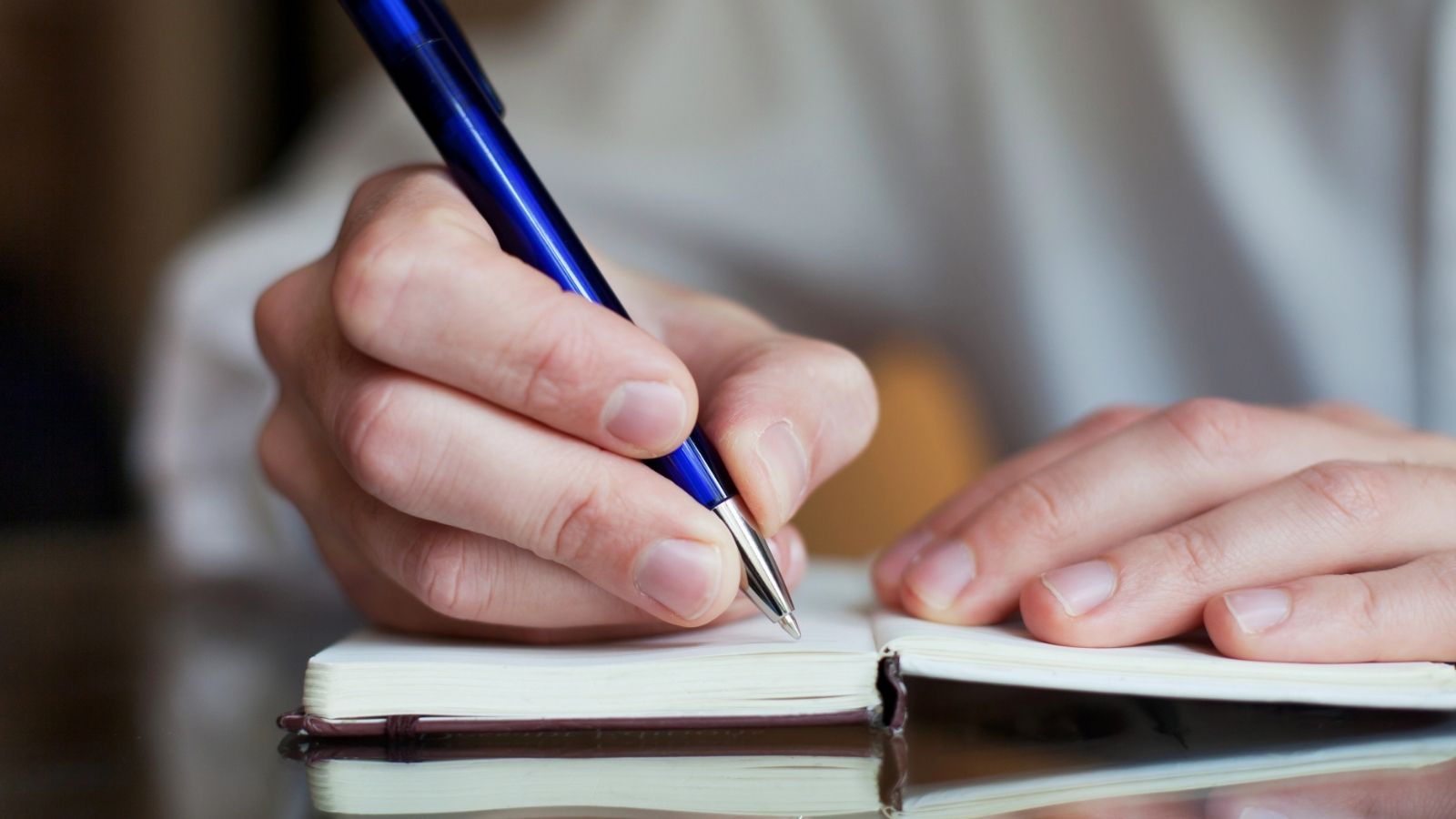 A person writing in a notebook with a blue pen, focusing on their hands and the open pages.