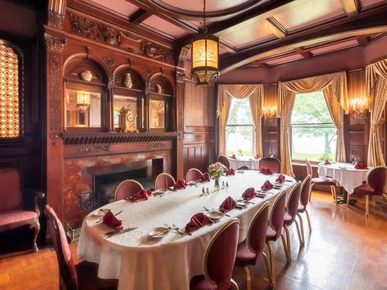 Elegant dining room with ornate wood paneling, a fireplace, and a long table set for a formal meal&mdash;reminiscent of the refined ambiances found at Finger Lakes wineries with lodging.