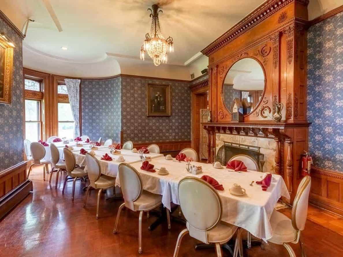 Elegant dining room with long tables, white tablecloths, chandelier, and ornate wooden fireplace mantel&mdash;perfect for guests seeking refined comfort at Finger Lakes Wineries with Lodging.