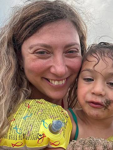 A woman and child taking a selfie on the beach with sand on their faces, enjoying quality time at one of the best family resorts.