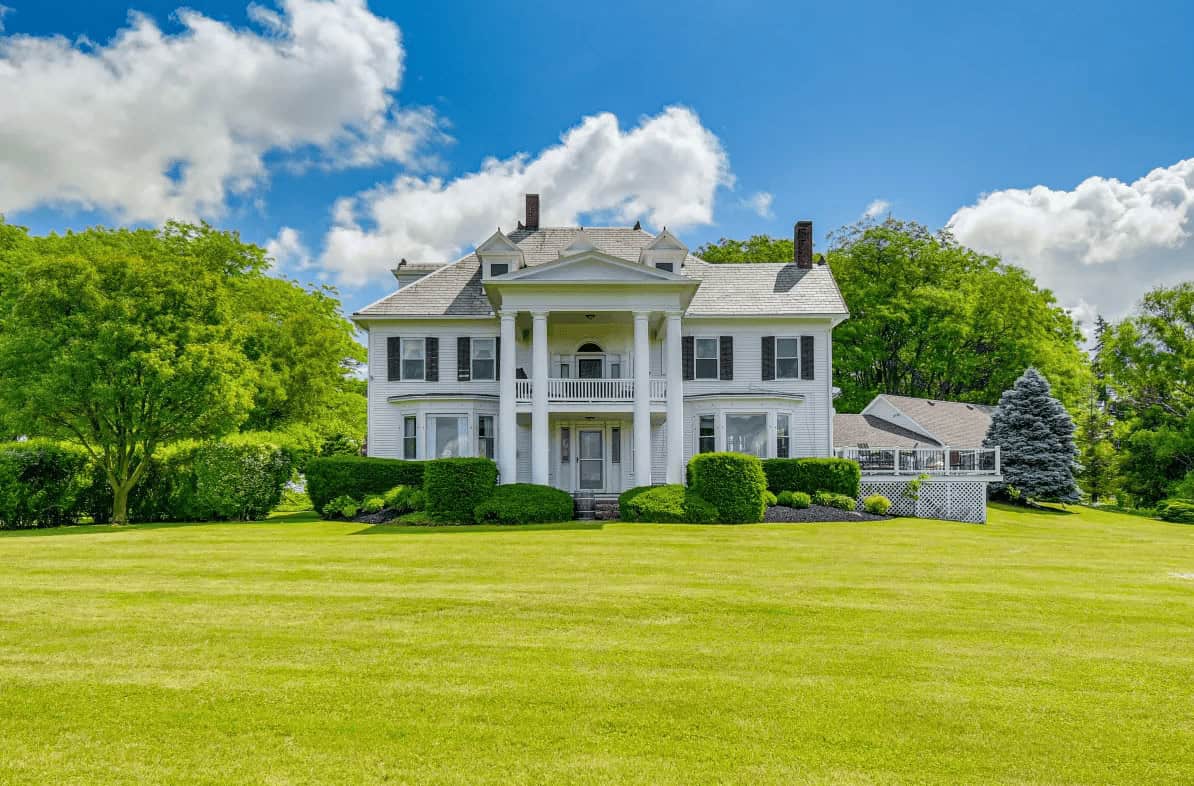 Elegant white colonial-style house with columns, set on a green lawn beneath a bright blue sky&mdash;an inviting retreat reminiscent of Finger Lakes Wineries with Lodging, perfect for relaxing amidst tranquil scenery.