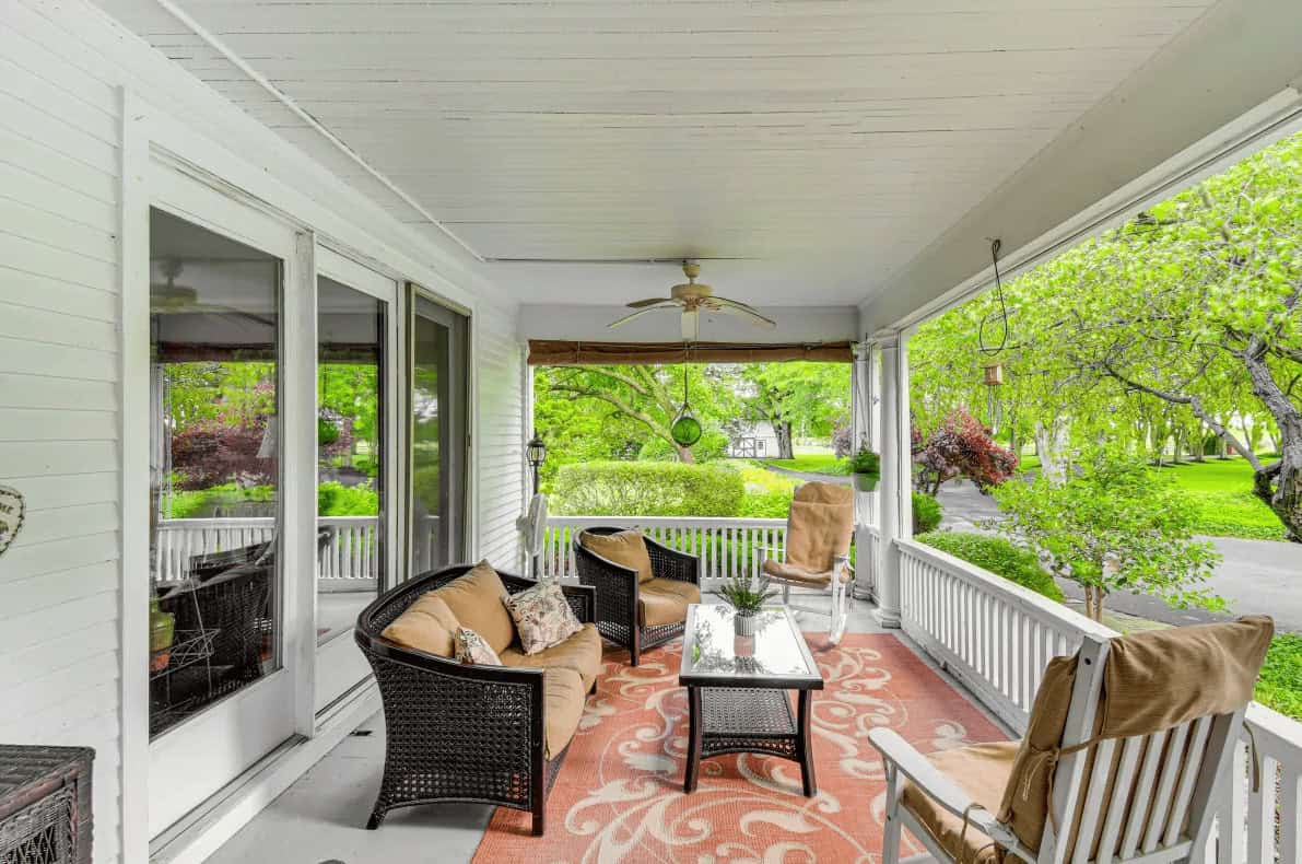 Cozy porch with wicker furniture, rug, ceiling fan, and lush green trees surrounding the space&mdash;perfect for relaxing after a day exploring Finger Lakes Wineries with Lodging nearby.