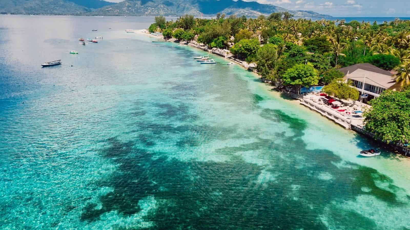 Aerial view of a tropical shoreline with clear blue water, boats, and lush green trees along the coast.