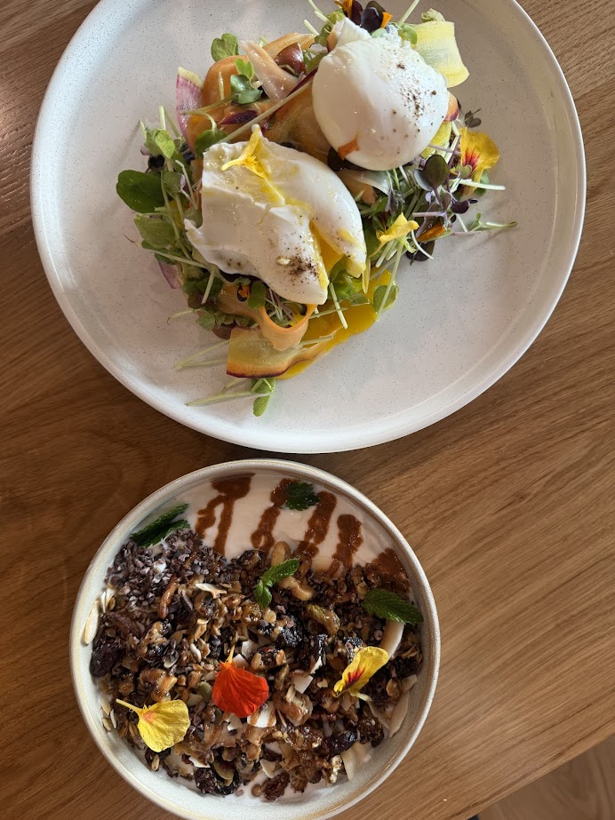 Two white plates: one with poached eggs on greens, the other with a colorful granola and fruit bowl—perfect fuel for a Finger Lakes weekend getaway.