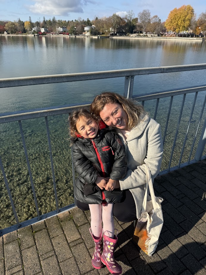 Woman and young girl smiling while hugging by a lakeside railing on a sunny day—perfect for a Finger Lakes weekend getaway.
