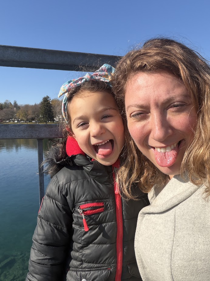 Woman and young girl smiling and sticking out their tongues by a lake on a sunny Finger Lakes weekend getaway.