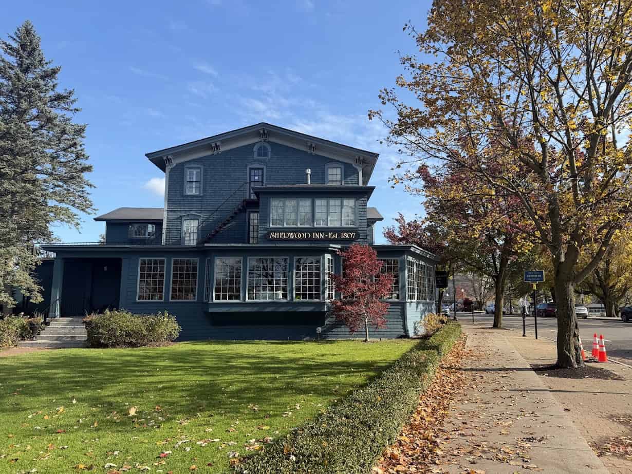 Blue historic building labeled "Sherwood Inn" with autumn trees and a green lawn in front—perfect for a fall road trip or relaxing weekend getaway in the scenic Finger Lakes region.