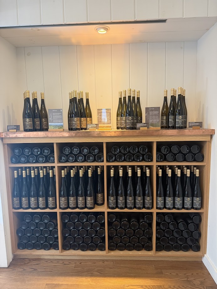 Wooden shelves display rows of wine bottles from some of the best wineries in Finger Lakes, arranged both upright and stacked horizontally.