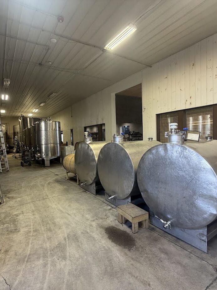 Large stainless steel tanks and barrels line the walls of a spacious, well-lit industrial room—an impressive sight often found at the best wineries in Finger Lakes.