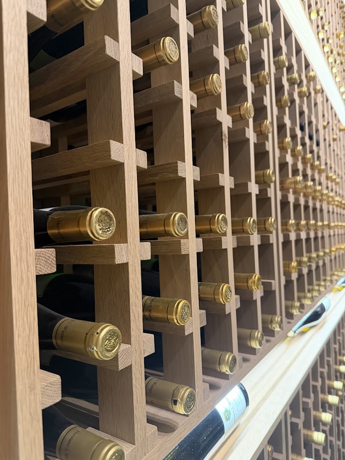 Rows of wine bottles from the best wineries in Finger Lakes are stored horizontally in a wooden wine rack, their gold foil tops facing outward.