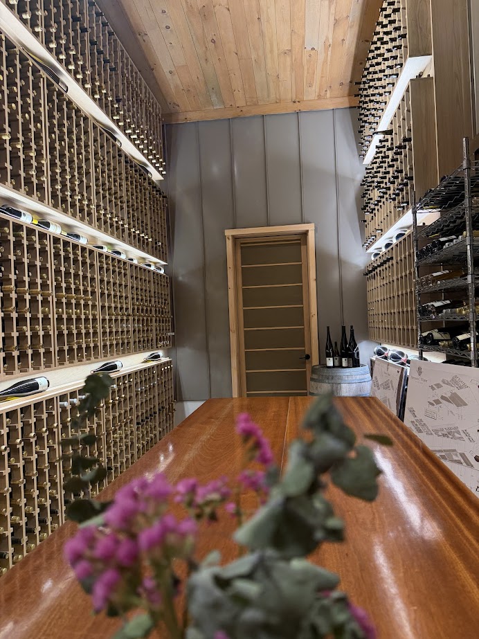 A wine cellar with wooden racks full of bottles, a wooden table, and flowers in the foreground—evoking the charm of the best wineries in Finger Lakes.
