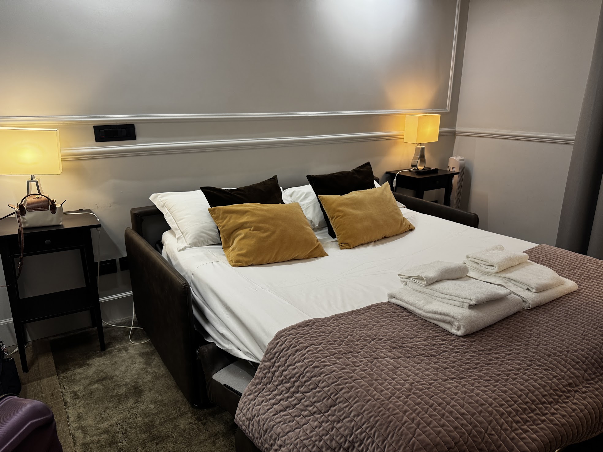 A neatly made bed with yellow and black pillows, bedside tables, lamps, and folded towels at the foot&mdash;perfect for relaxing during your family vacation at one of the best family resorts.