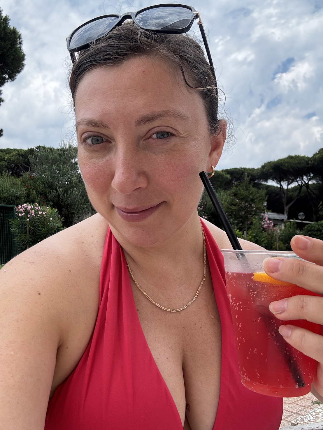 Woman in a red halter swimsuit holding a pink drink with orange by the pool, enjoying the sun at one of the best family resorts, sunglasses perched on her head.