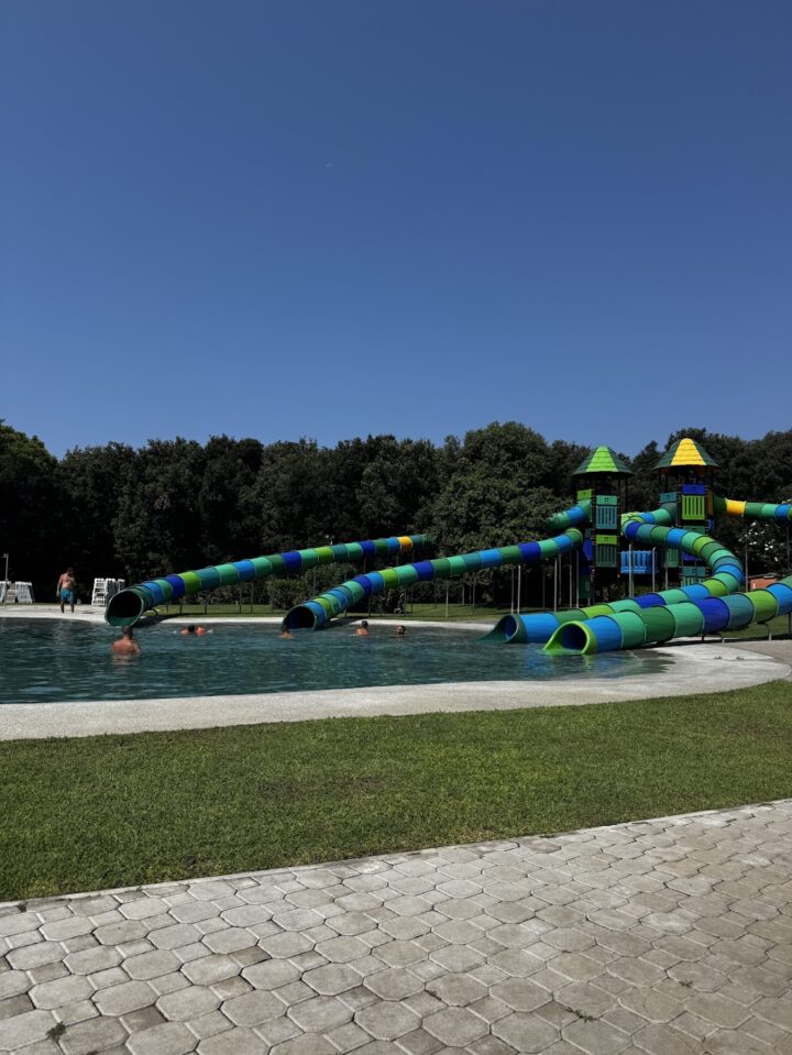 Outdoor pool with colorful water slides, green grass, and people swimming under a clear blue sky&mdash;perfect for memorable days at one of the best family resorts.