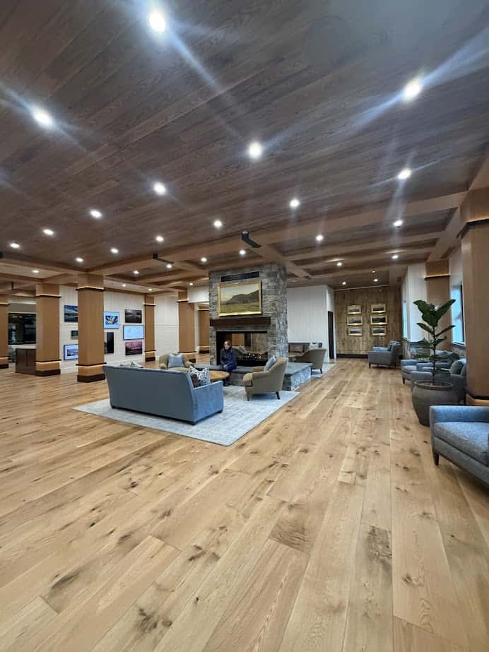 Spacious lobby with wood floors, modern furniture, stone fireplace, and a person sitting on a sofa—welcoming comfort at Skaneateles Fields Resort & Spa in the heart of the Finger Lakes.
