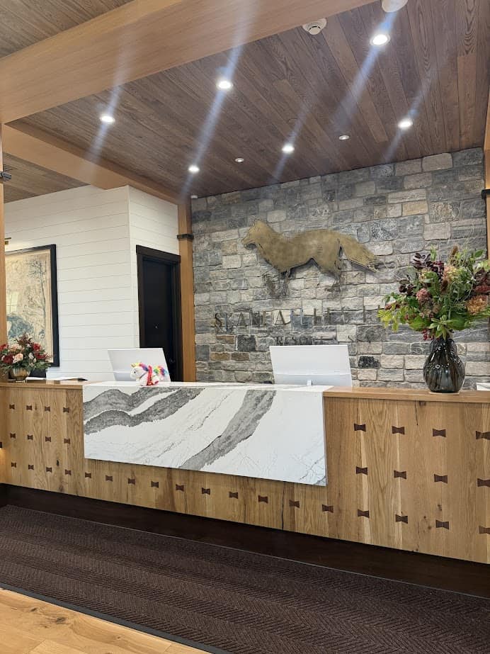 Reception desk with marble detail, floral arrangements, and a large fox sculpture on a stone wall behind, welcoming guests to the tranquil ambiance of Skaneateles Fields Resort & Spa in the heart of the Finger Lakes.