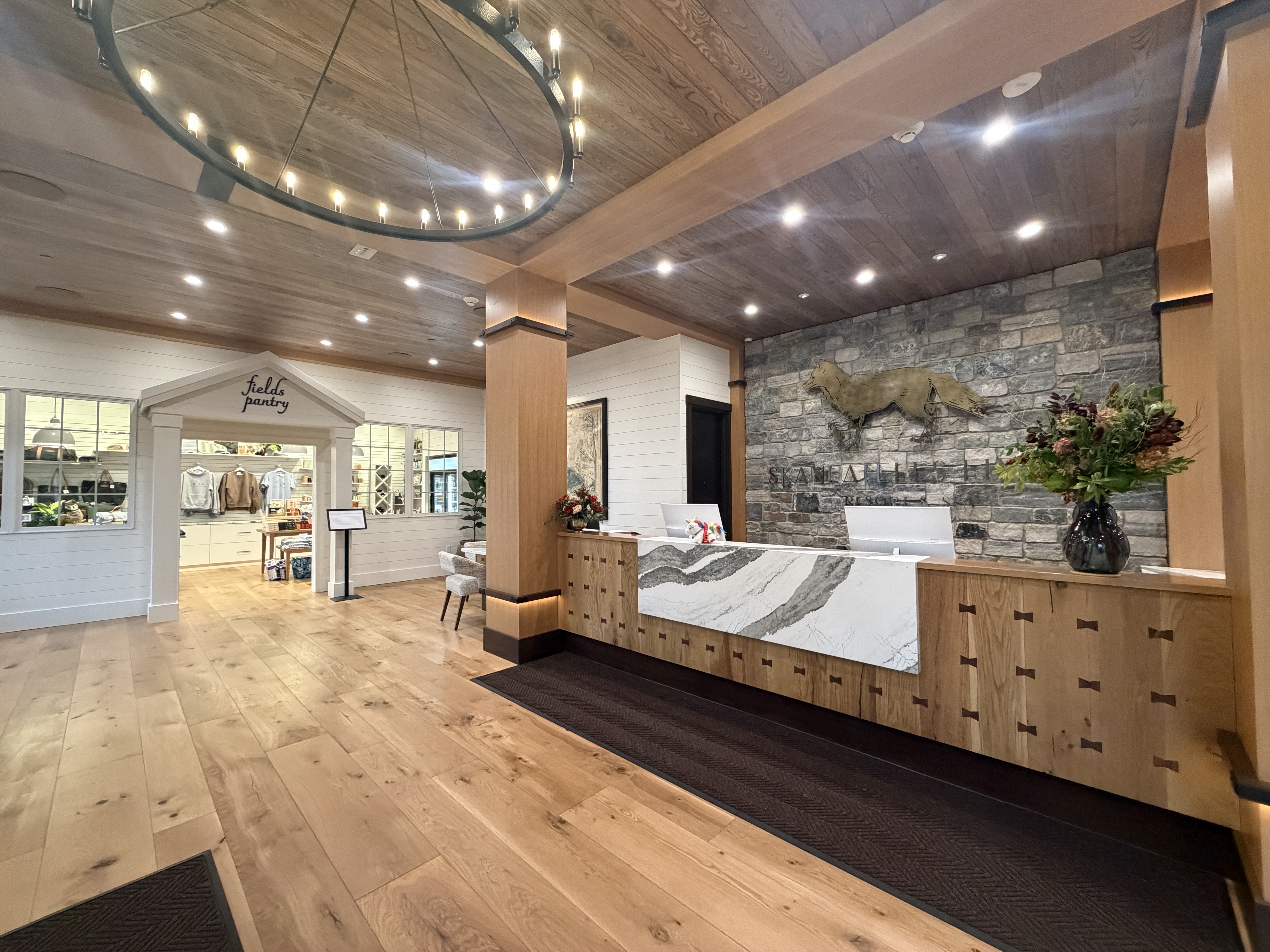 The Hotel lobby at Skaneateles Fields Resort features a marble reception desk, wood floors, stone wall accents, and a gift shop entrance on the left—offering guests a welcoming introduction to the Finger Lakes experience.