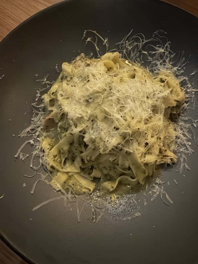 A plate of tagliatelle pasta topped with shredded cheese, served on a dark dish at Skaneateles Fields Resort, offers a taste of the Finger Lakes region’s culinary charm.