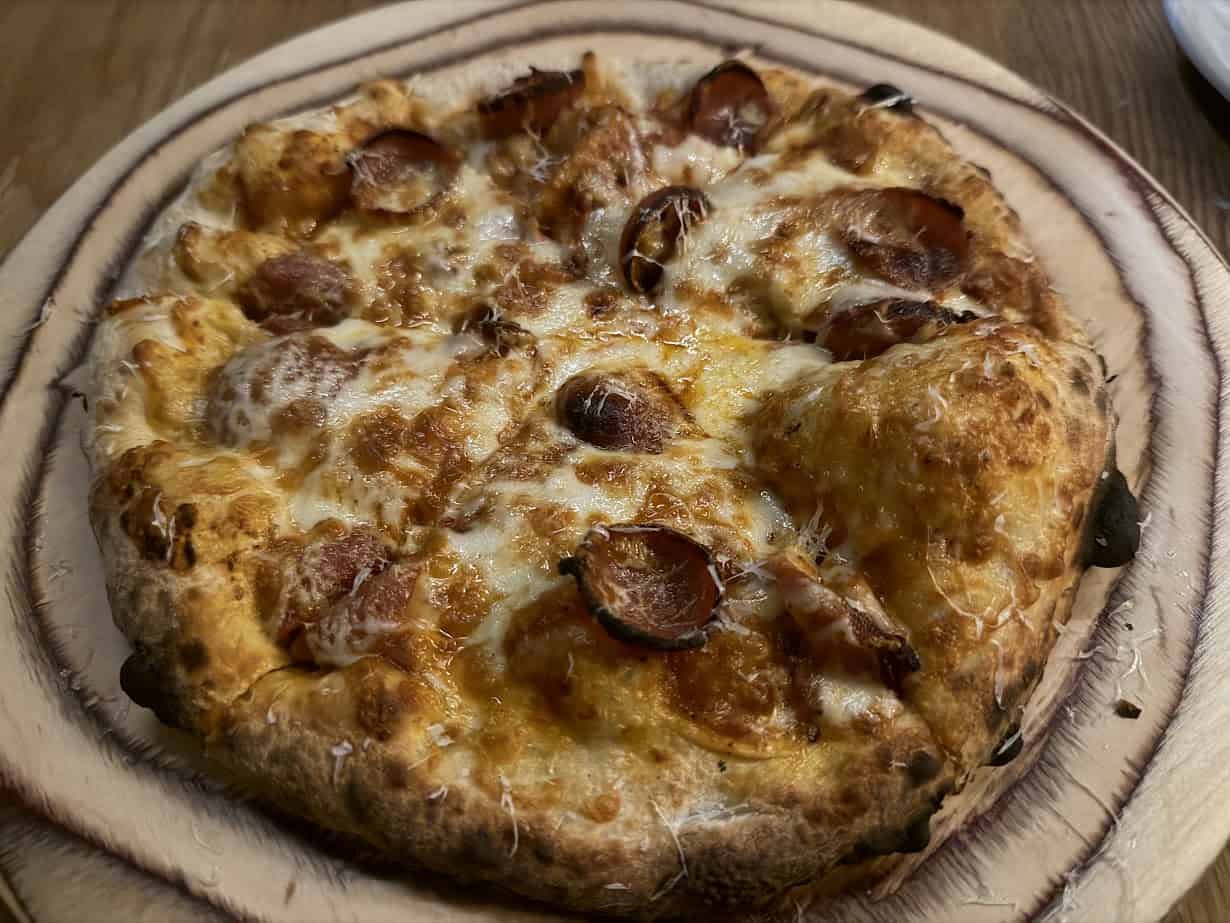 A freshly baked pepperoni pizza with melted cheese on a wooden serving board, perfect for enjoying after a relaxing spa day at Skaneateles Fields Resort in the scenic Finger Lakes.