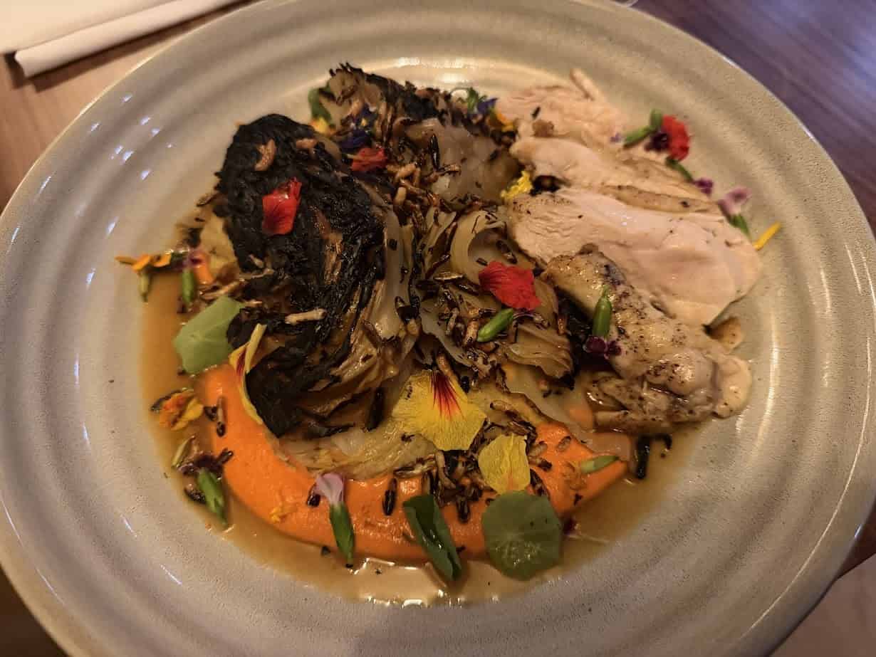 Roast chicken with charred cabbage, edible flowers, and sauce on a ceramic plate—an artful dish inspired by the serene ambiance of Skaneateles Fields Resort & Spa in the heart of the Finger Lakes.