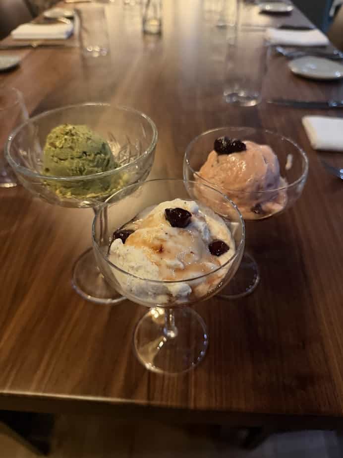 Three glass dishes of ice cream—green, pink, and white with berries—sit on a wooden table set for dining at Skaneateles Fields Resort & Spa in the scenic Finger Lakes.