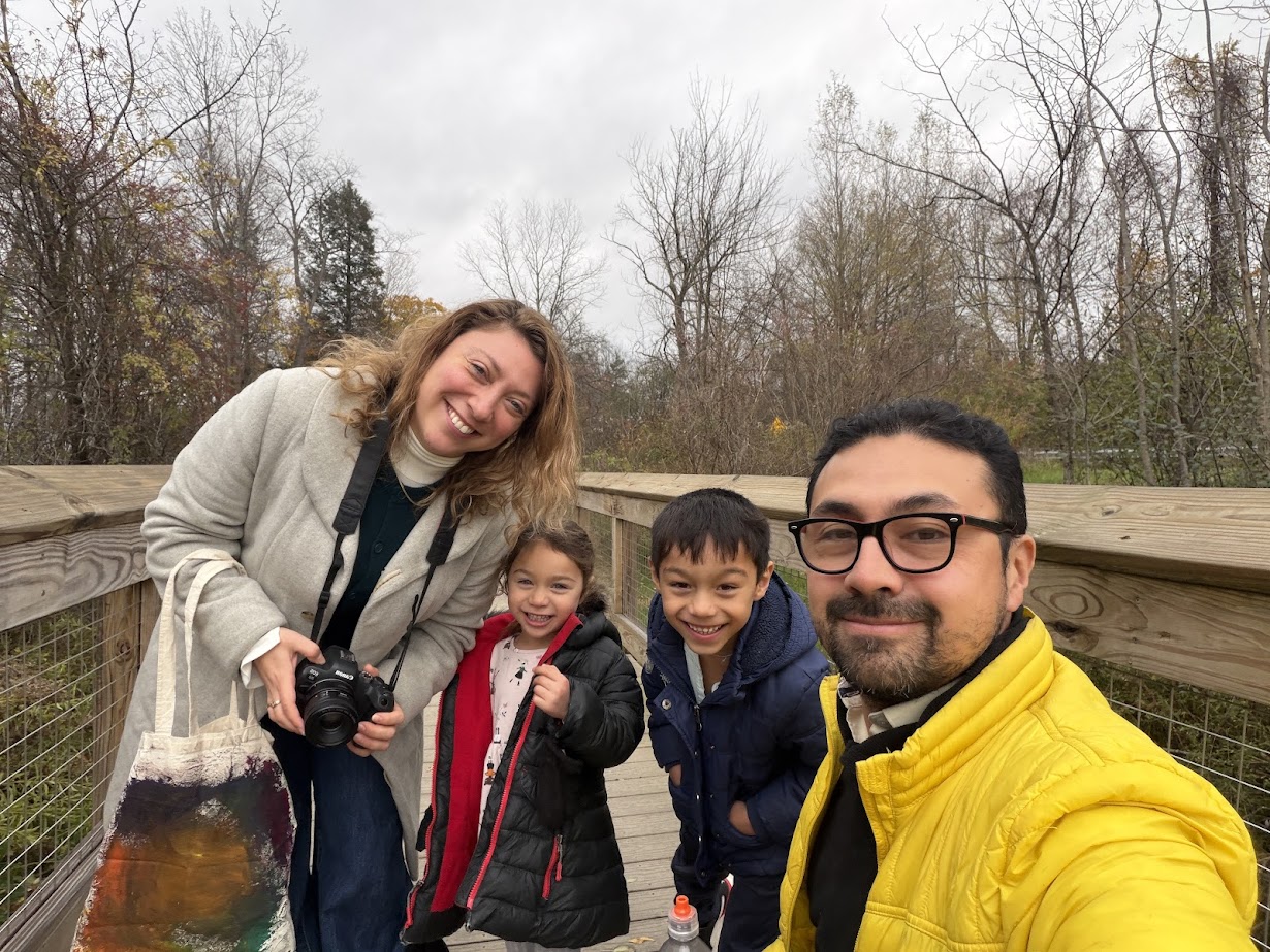 Four people smile on a wooden walkway outdoors at Skaneateles Fields Resort in the Finger Lakes; two adults and two children pose for a cheerful group selfie, capturing memories after a fun day at the spa.