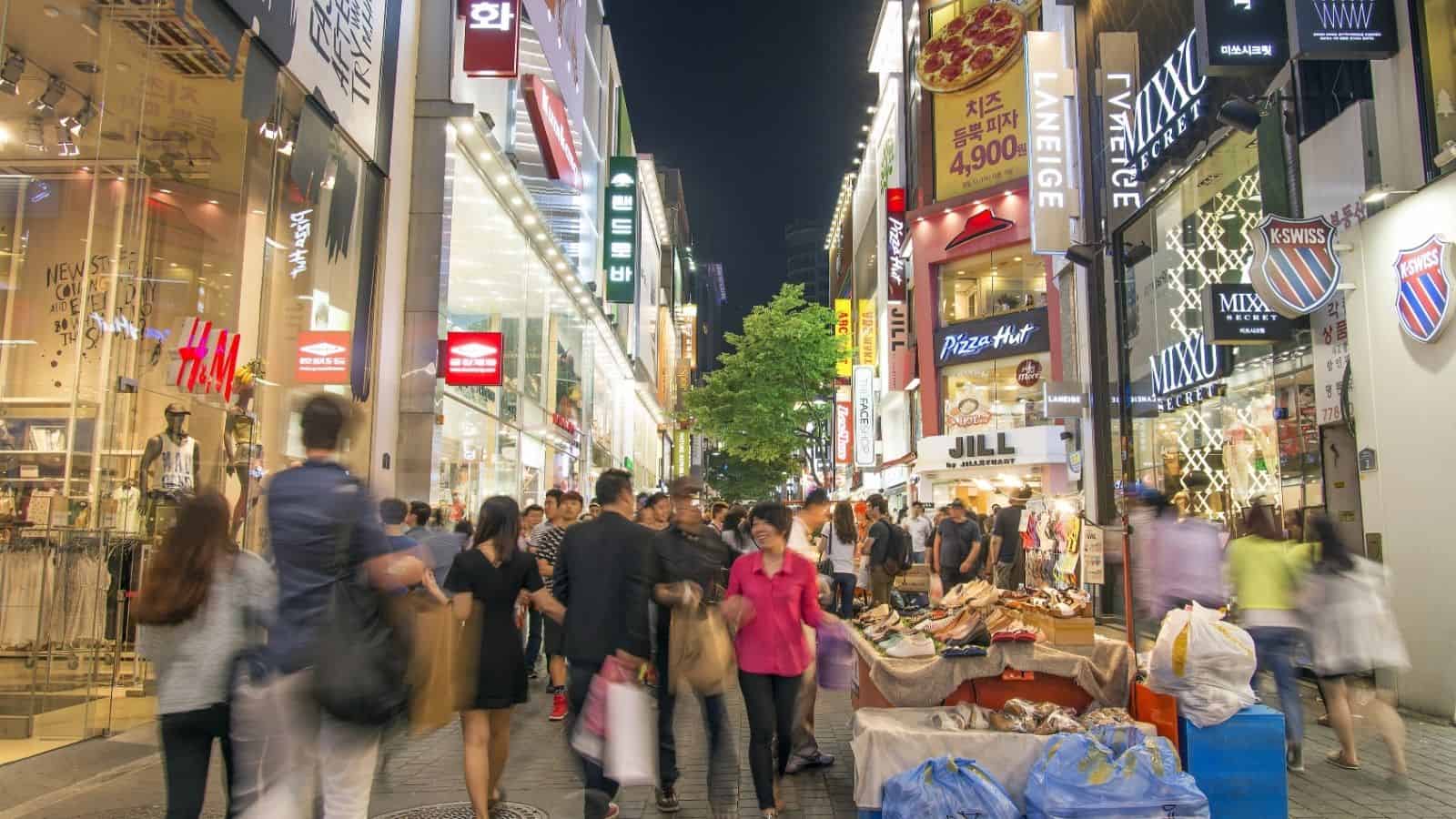 Busy city street at night with people shopping and colorful store signs lighting up the scene.