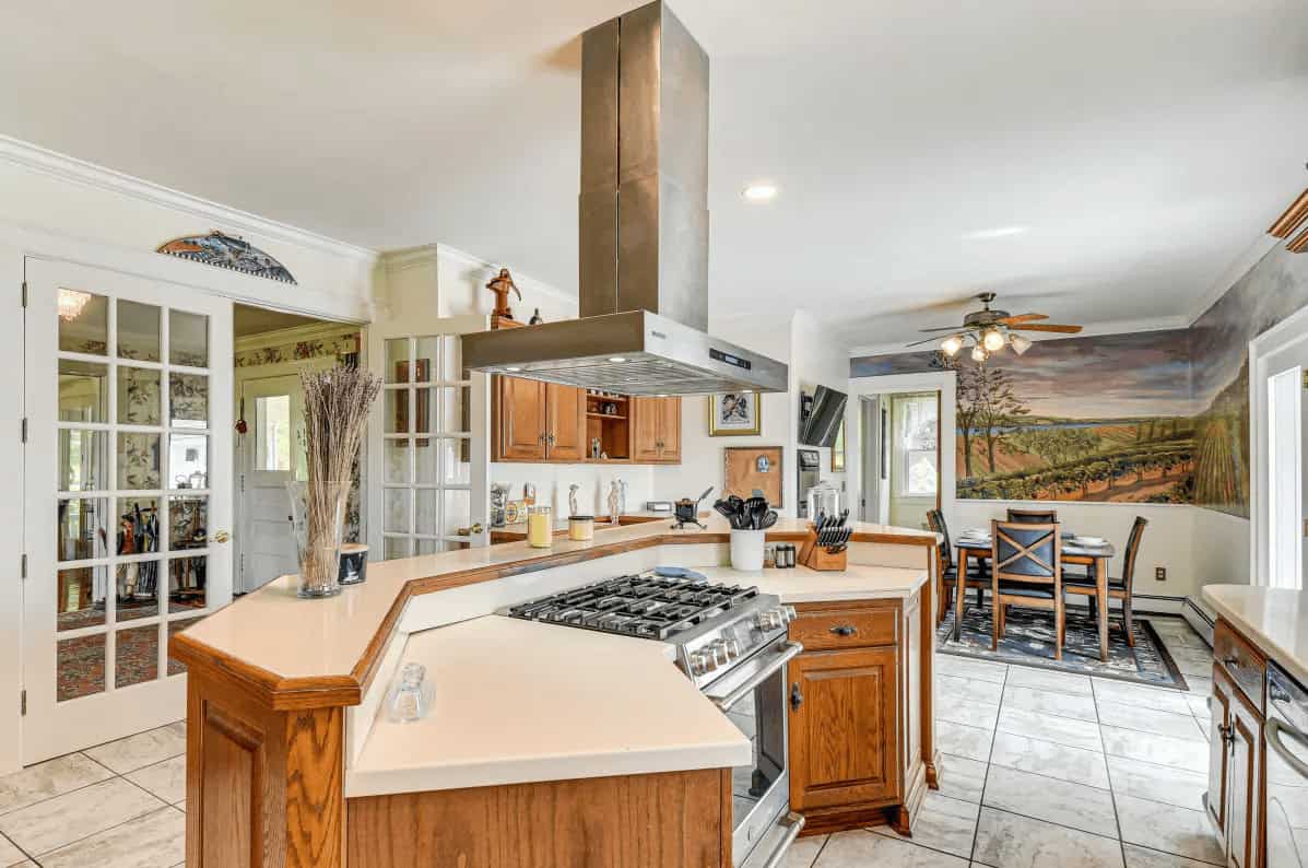 Bright kitchen with wooden cabinets, central stove, and a dining area featuring a mural of a vineyard scene&mdash;evoking the ambiance of Finger Lakes Wineries with Lodging.