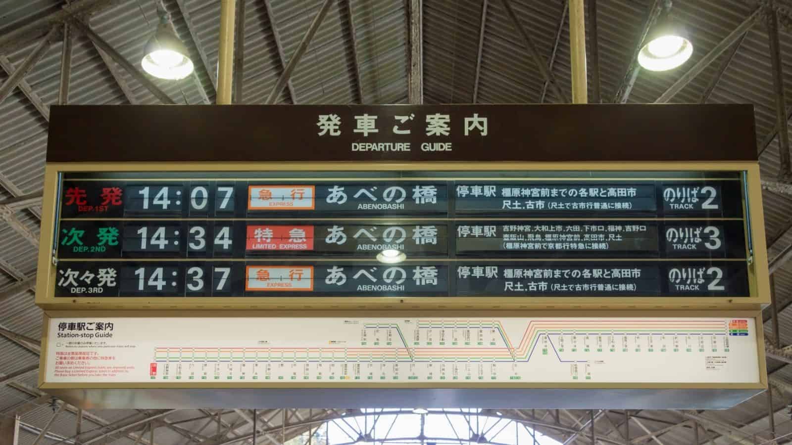 Japanese train station departure board with digital schedules and a route map displayed above the platform.