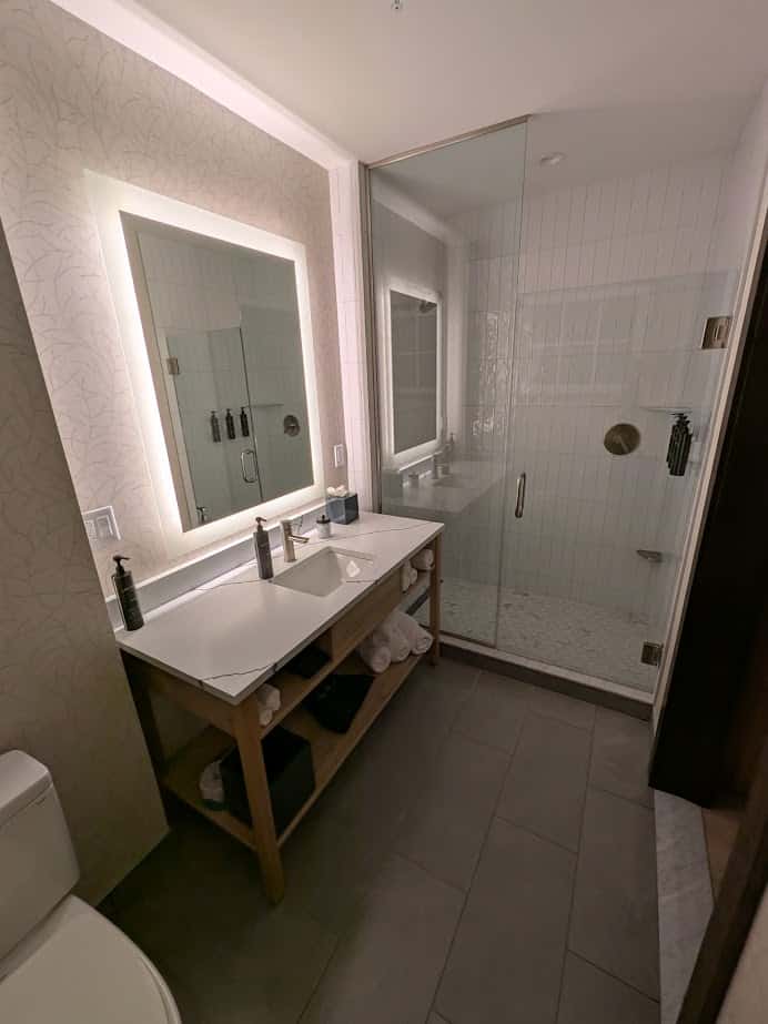 Modern bathroom with a spa-like ambiance featuring a backlit mirror, sink, wooden vanity, and glass shower enclosure—perfect for relaxing after a day at Skaneateles Fields Resort in the Finger Lakes.