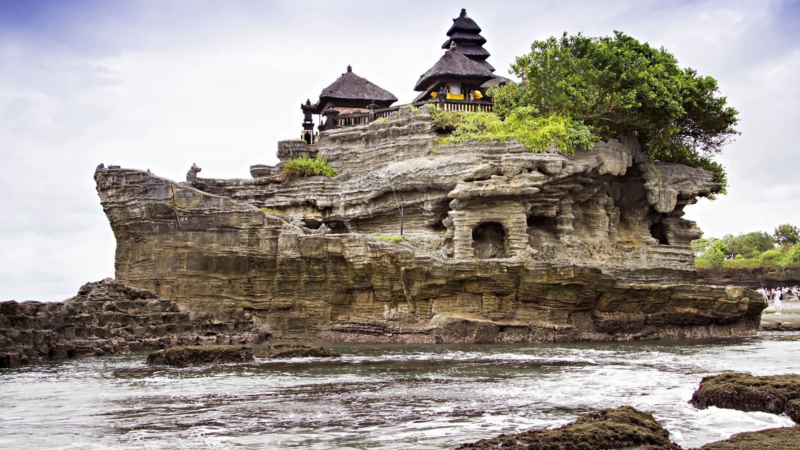 Balinese temple perched atop a rocky seaside cliff with waves below and greenery above—a must-see for those seeking Asia travel tips or planning hot weather travel adventures.