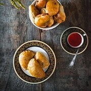 A plate and bowl of baked pastries—a nod to vegetarian dishes in Russia—served with a cup of tea and a teapot on a rustic wooden table, flowers beside.